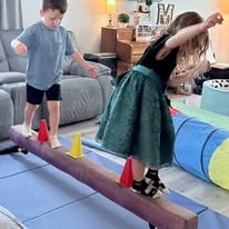 Two children balancing on a balance beam with colorful cones in a playroom