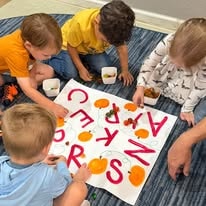 Toddlers playing with alphabet letters and pumpkin cards on an activity mat