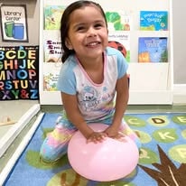 Smiling girl sitting on a pink bouncy ball in a classroom