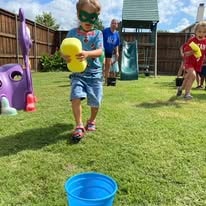 Child playing a backyard game tossing a ball toward a blue bucket
