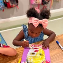 Young girl with a pink bow painting a craft project at a table