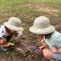 Two children in safari hats examining nature with a magnifying glass