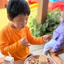 Child in an orange shirt eating cake and snacks at a birthday celebration