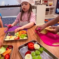 Child in chef hat preparing fruit snacks at a table