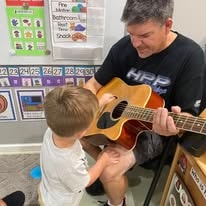 Teacher playing guitar with a young child in the classroom