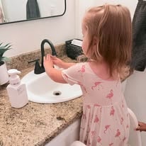 Toddler in a pink dress washing her hands at a bathroom sink