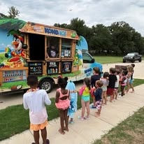 Children lined up at a colorful Kona Ice shaved ice truck