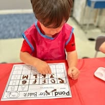 Child in a pink apron matching letters on an activity worksheet