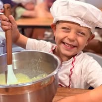 Smiling child in chef hat and apron stirring batter in a large bowl