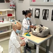 Children in white lab coats playing veterinarian with stuffed animals in a play clinic