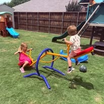 Two children riding a seesaw in the backyard playground