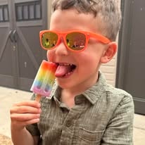 Boy in orange sunglasses enjoying a rainbow popsicle