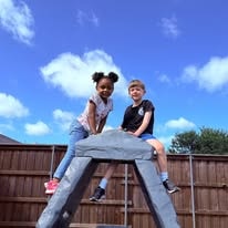 Two children climbing on an outdoor play structure under a blue sky