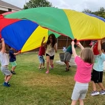 Teacher and children holding a colorful rainbow parachute outdoors