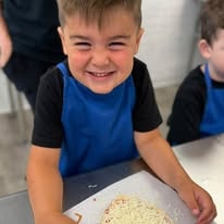 Smiling boy in a blue apron with his pizza in front of him
