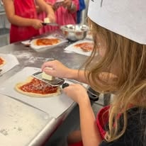 Child in a chef hat grating cheese onto a pizza