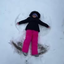 Child in black jacket and pink pants making a snow angel in the snow