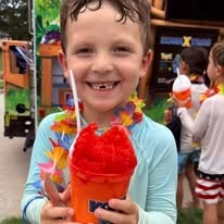 Smiling child holding a red snow cone with a flower lei