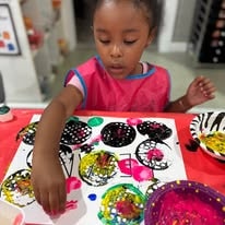 Child in a pink apron creating colorful spin art at a table