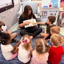 Teacher reading a book to a group of young children on the floor