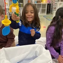 Smiling child in a classroom playing with a toy drill and colorful bag
