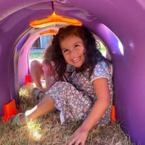 Smiling girl sitting inside a purple play tunnel outdoors