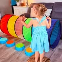 Toddler in a light blue dress playing with a rainbow tunnel and colorful stepping stones