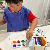 Child in a blue smock painting with watercolors at a table