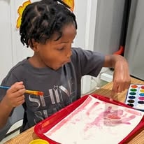 Child painting with watercolors at a red art tray