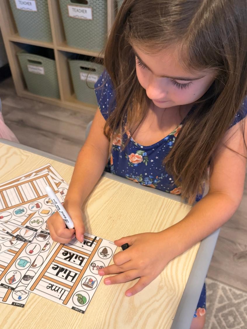 Girl writing words with a dry-erase marker on phonics activity cards
