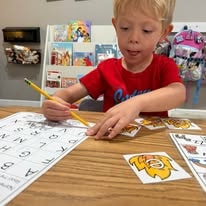 Young boy in a red shirt practicing writing letters on a worksheet at a table