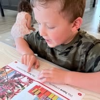 Young boy pointing at letters on printed learning cards at a table