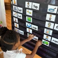 Young child placing word cards on a classroom word-wall chart